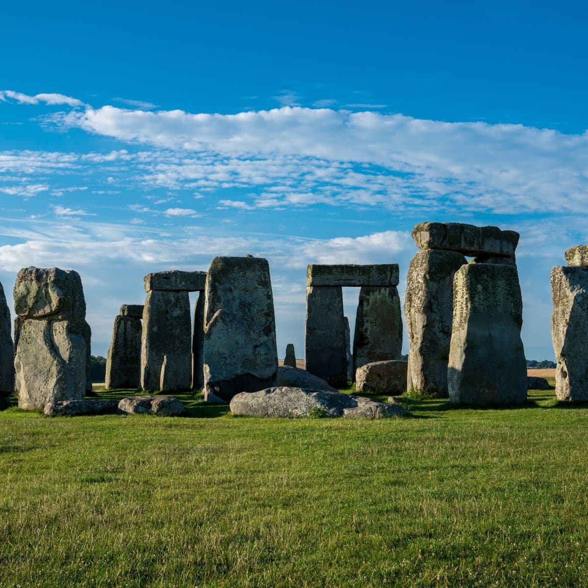 Ancient stone structure at Stonehenge under a blue sky with scattered clouds, surrounded by a grassy field.