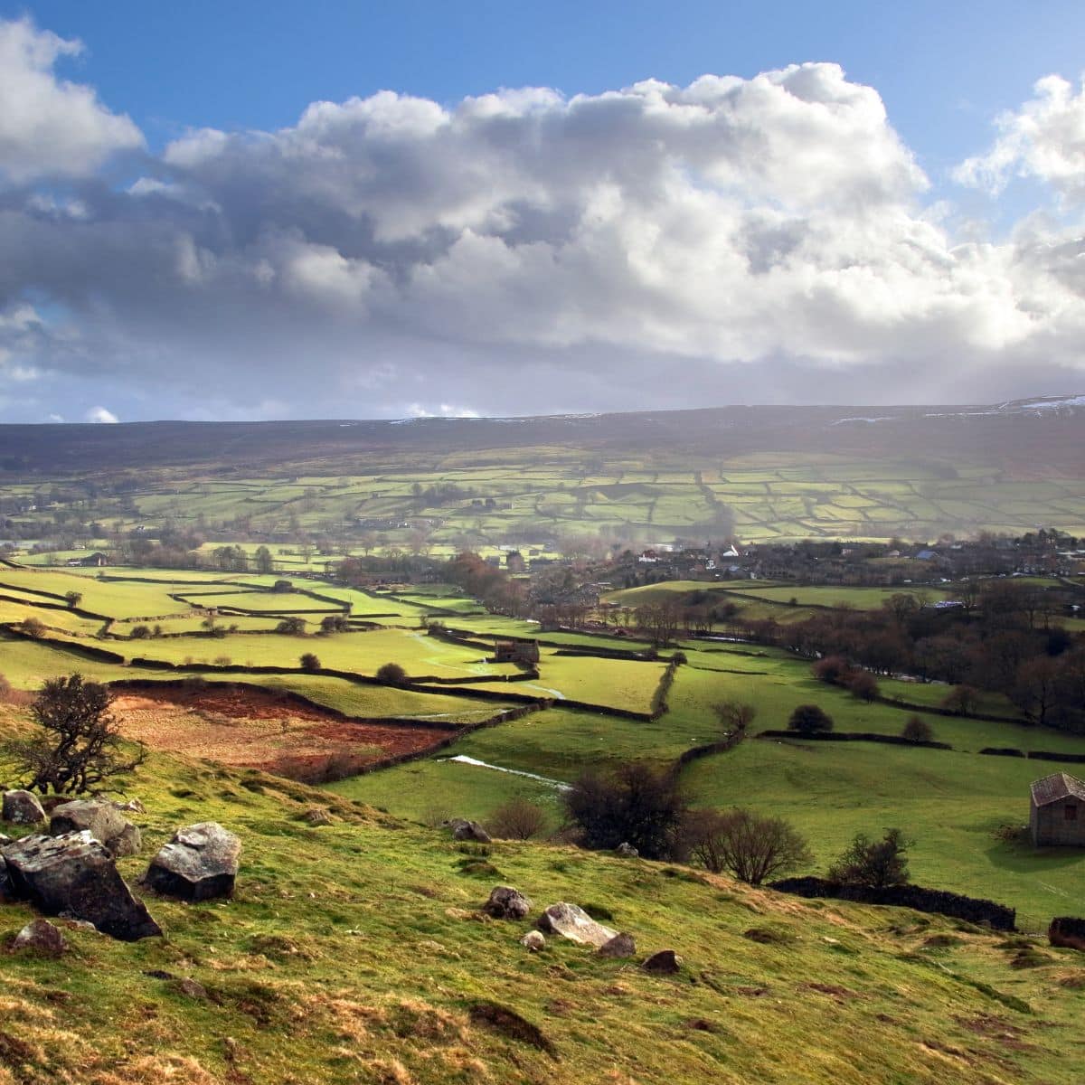 Rolling green fields and stone-walled pastures stretch across a rural landscape under a partly cloudy sky.