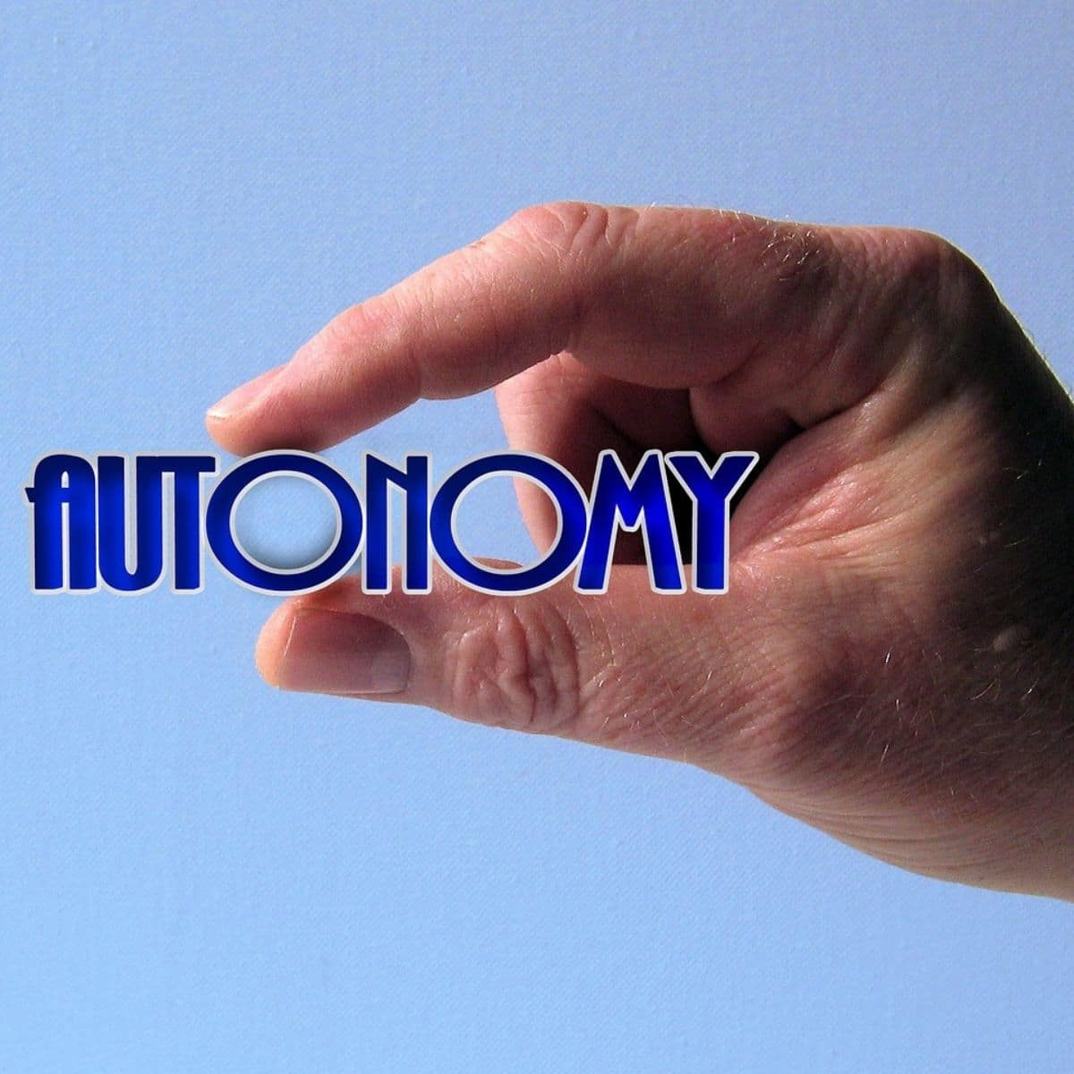 A hand holds its fingers close together, appearing to pinch the word "AUTONOMY," which is written in bold blue letters against a light blue background.