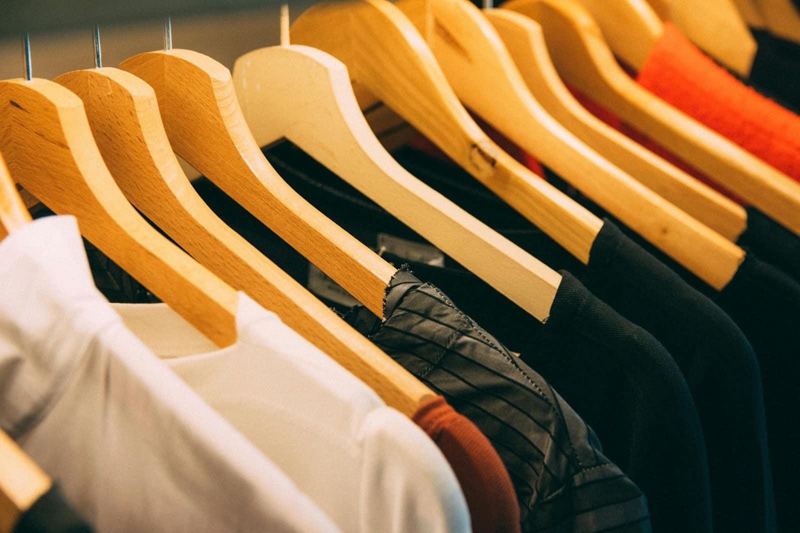 Row of wooden hangers holding assorted clothing items, including shirts and jackets, on a clothing rack.