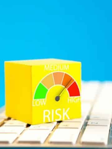 A yellow cube labelled "RISK" with a gauge pointing to "HIGH" sits on a computer keyboard, against a blue background.