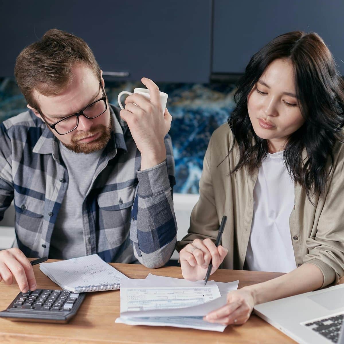 Two people sit at a table reviewing documents with a calculator and notebook, appearing focused and engaged in paperwork.