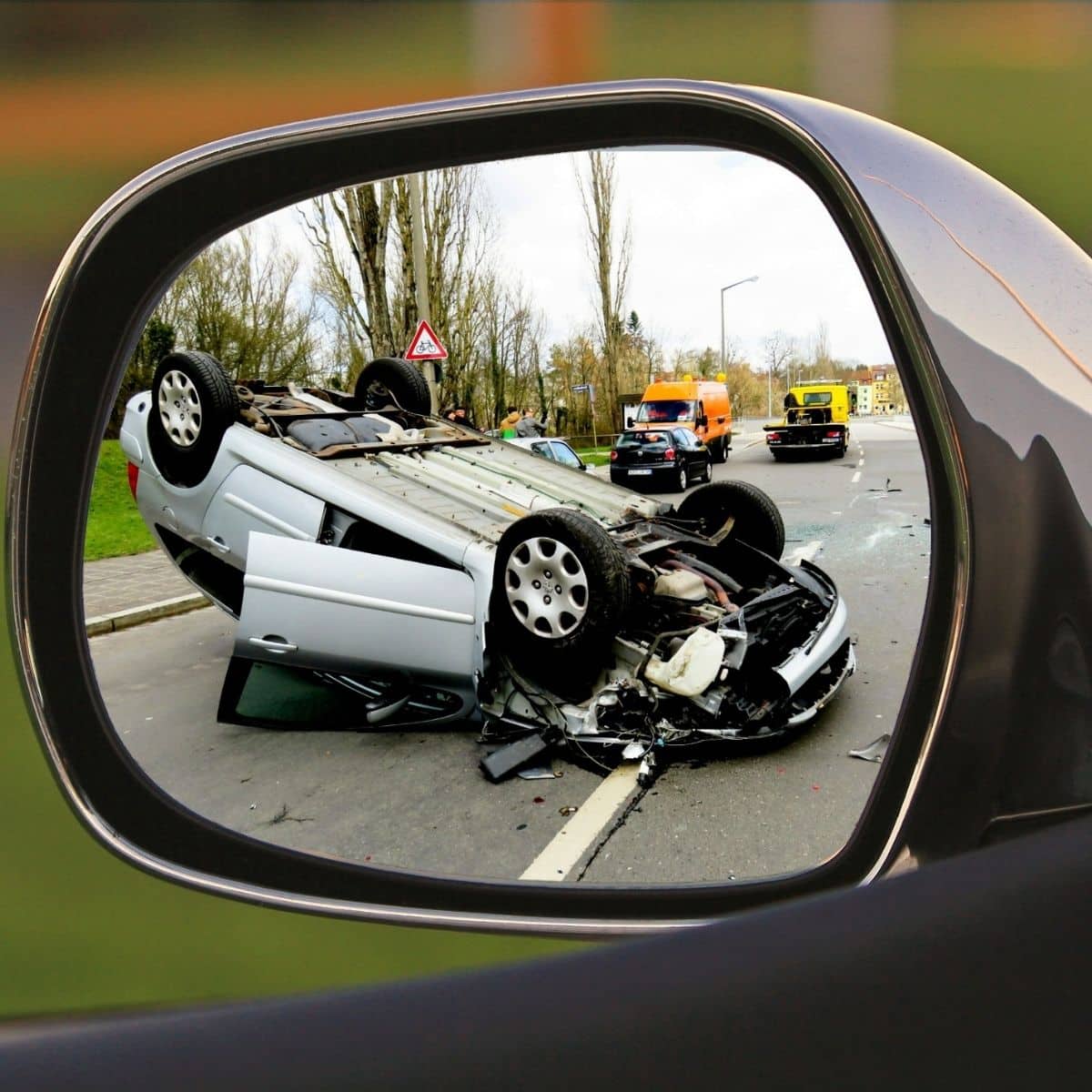 Car Accident Dream Meaning. A overturned car with severe damage is seen in a wing mirror, with emergency vehicles and people present at the scene of the accident on the road.