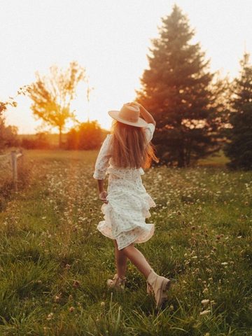 Self Motivation Intentional Quotes to Inspire Best Living 7 A person in a white dress and hat walks through a grassy field at sunset, surrounded by trees and wildflowers.