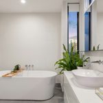 Creating a Spa-Like Bathroom Retreat at Home 1 Modern bathroom with a freestanding bath, vessel basin on a white vanity unit, towels, a large plant, and a window showing an evening sky.