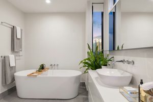 Creating a Spa-Like Bathroom Retreat at Home 14 Modern bathroom with a freestanding bath, vessel basin on a white vanity unit, towels, a large plant, and a window showing an evening sky.